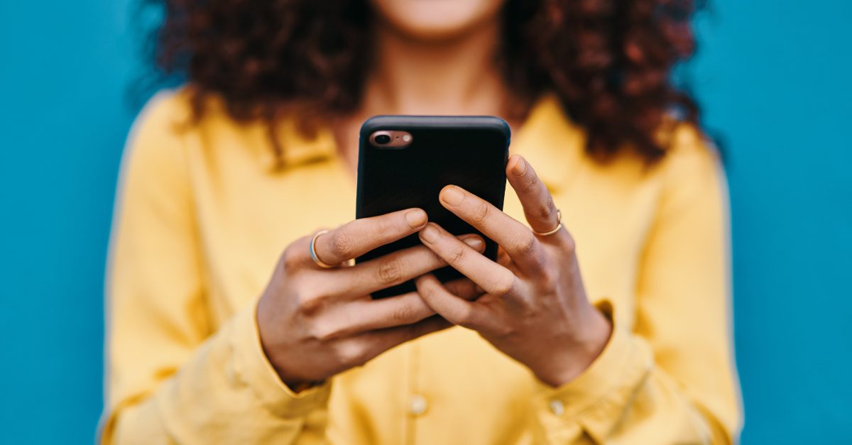 woman with curly hair in yellow shirt looking at smartphone