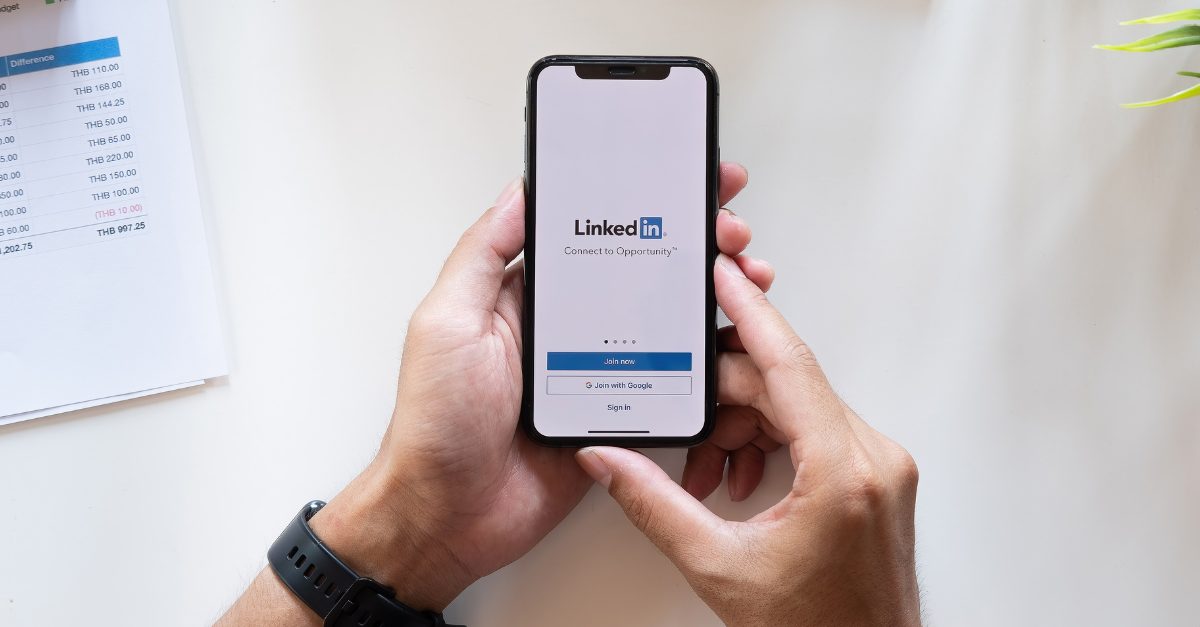 man's hands holding smartphone looking at linkedin