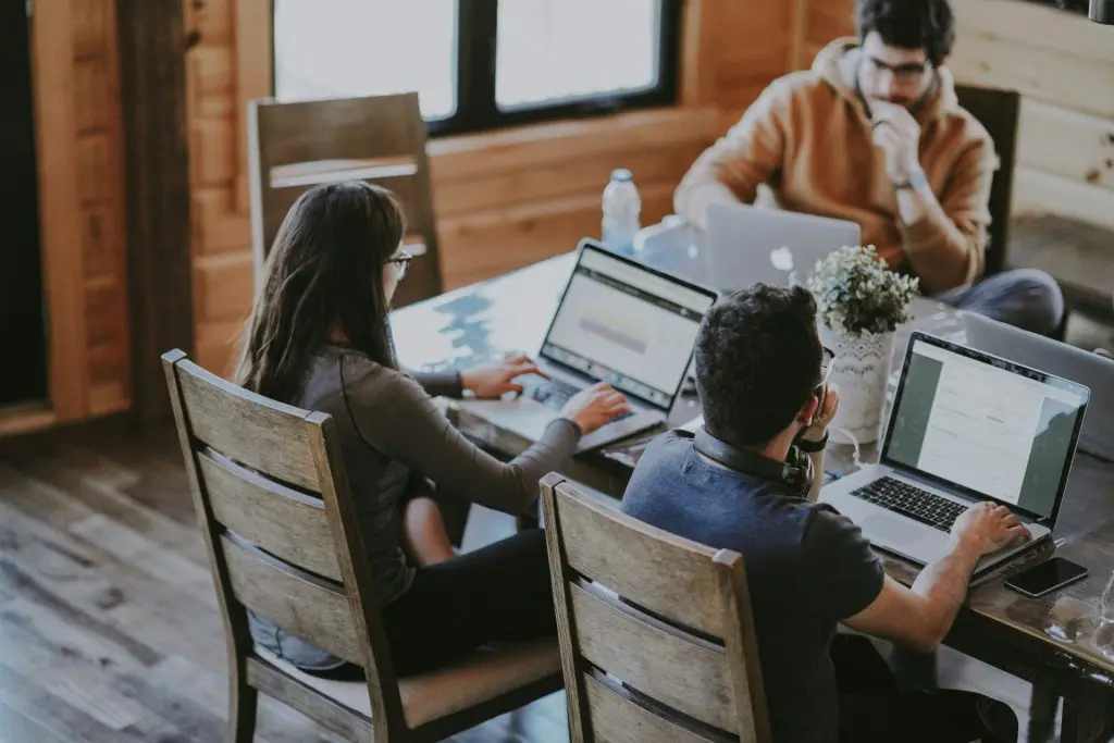 people working at a table on their laptops sitting in wooden chairs